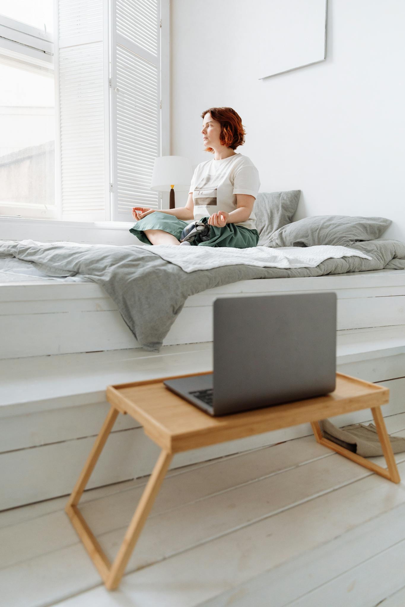 Woman practicing meditation on bed by window, embracing tranquility indoors.